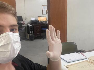 White male researcher showing a gloved hand and wearing a white ply mask as he handles archival documents.