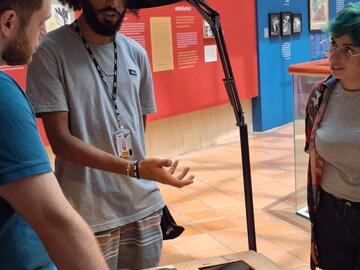 Three people discussing museum items at an exhibition in São Paulo.