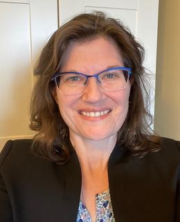 Female with medium length brown hair and blue glasses.