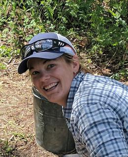 A photo of Dr. Lindsay Amundsen-Meyer in the field. She is wearing a baseball cap and plaid shirt and smiles at the camera.