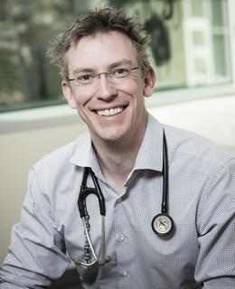 Photo of David Keegan, sitting down in clinic with a stethoscope around his neck.