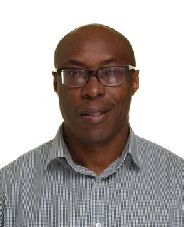A headshot photo of Dr. Uchechukwu Umezurike. He wears glasses and a gray shirt, against a white background. 
