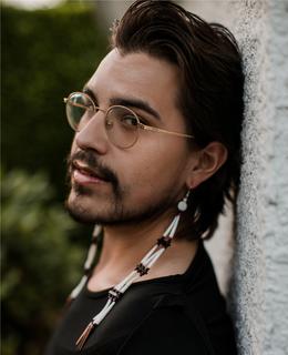 Profile photo. Author is against the wall wearing a black shirt and earrings.