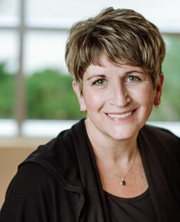 Photograph of Joelle Welling wearing a black cardigan over a striped t-shirt.