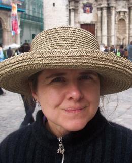 White woman wearing a large straw hat and a black sweater in a courtyard in Havana.