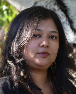 A headshot of Dr. Banerjee wearing a black blazer, hair down, by a tree. 