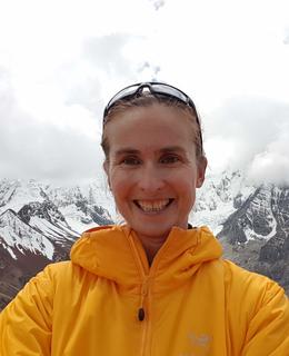 Woman wearing a bright yellow jacket with mountains in the background.