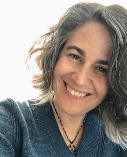 A photo of Dr. Jenny McKenney. She has shoulder-length hair, and wears a blue sweater and a necklace.