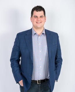A photo of David Sigler. He has short hair, and wears a navy-blue jacket and blue striped shirt, against a white background.