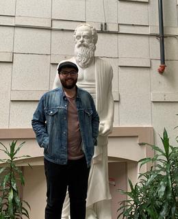 Tyler Wark standing beside a statue of Socrates