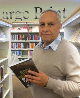 A man holding an open book is looking to the camera
