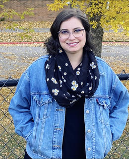 A young woman stands in front of a chain link fence
