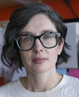 white woman with dark hair and glasses sits in front of computer screen