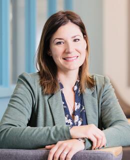 Photo of Victoria Fast; she has brown hair and brown eyes, is seated, and wearing a green jacket.