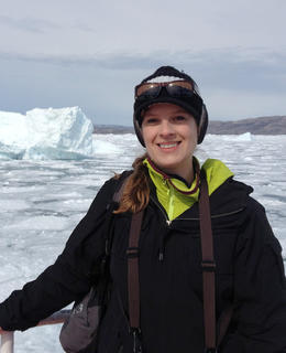 Dr. Kristine Thoreson on a boat in Greenland, iceberg behind.