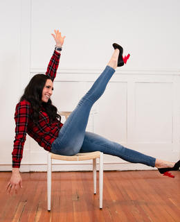 Danaka balances in a chair, her arms outstretched so her legs can be up in the air. Her shoes are made of lightening bolts