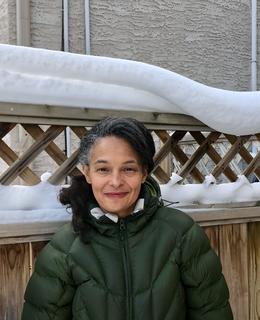 Woman in green puffer coat in front of fence with snow