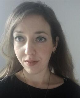 Closeup of Dr. Anna Veprinska, a woman with long dark blonde hair, wearing black, against a gray background.