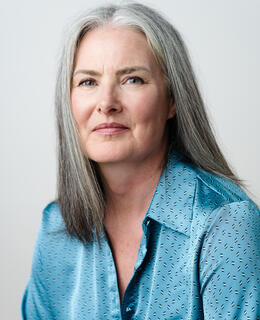 Female-identifying, grey, shoulder length hair, blue shirt