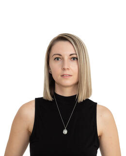 Portrait of woman with medium length blond hair wearing a black shirt against a bright white background. 