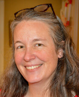 White woman with long grey hair and glasses on her head smiling.
