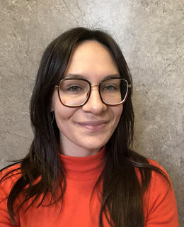 A woman with long dark hair and large brown glasses in a red turtle neck sweater.