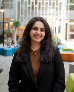 This is a photo of Zaara, wearing a brown top and black blazer. 