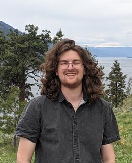 Masculine presenting person with glasses in a dark grey button up short sleeve