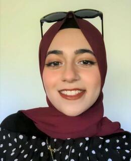 A photograph of Hafsa Maqsood. A woman smiling, wearing a dark red headscarf. 