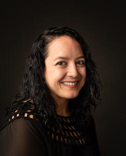 A photo of Tia wearing black in front of a dark background