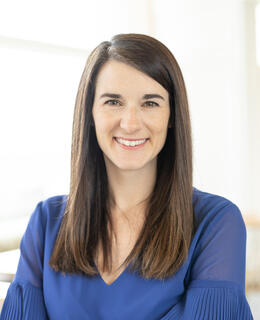 A woman with long brown hair, smiling, and wearing a blue dress