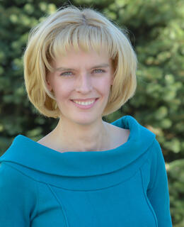Caucasian women with short blonde hair and blue eyes, wearing a blue long-sleeved shirt