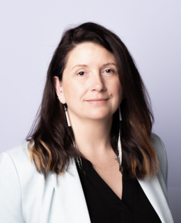 A photo of a woman with brown hair and a green blazer and black top in front of a white background