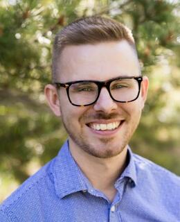 Liam wearing glasses and a blue shirt with trees in background