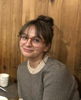 Image of Emily Howe sitting in front of a wood paneled wall, smiling.