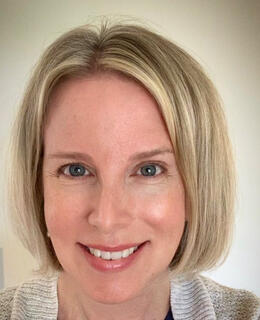 White woman with blonde hair and blue eyes wearing a beige sweater 