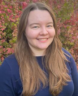 Headshot of a white woman with long light brown hair with leaves in the background