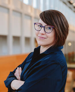 Headshot of a white woman with glasses and short hair standing in the Taylor Institute. 