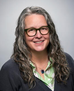 White woman with long grey hair and glasses.