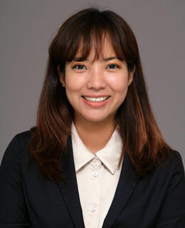 Sakura smiling in front of a grey background wearing a white shirt and black jacket.