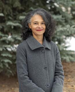 Suzette Mayr in grey coat in front of pine trees