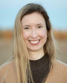 Smiling woman with sandy blonde hair, wearing brown shirt with camel cardigan