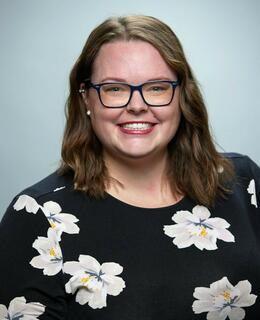 Caitlin is smiling at the camera, wearing a black dress with large white flowers