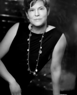 Vanessa Porteous sitting on the floor in a dark dress and a long necklace.