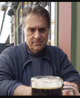 A man in a blue sweater staring intensely at a beer stein