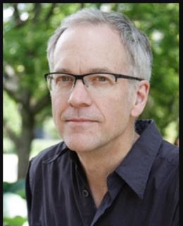 A man in black rimmed glasses, wearing a black collared shirt