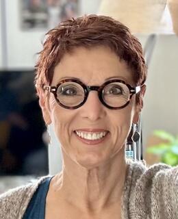 Lissa, smiling facial image, round glasses, short hair.