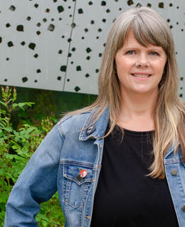 A middle-aged white woman with blonde hair wearing a jean jacket.
