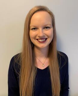 Photo of Leah, who has long blonde hair and is smiling at the camera. She is wearing a dark blue sweater.