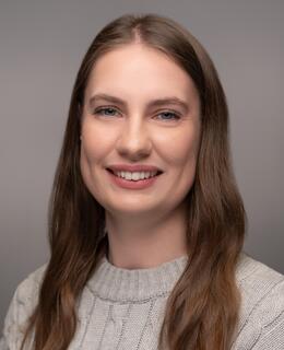 Headshot of Lindsay, she is smiling at the camera sitting at an angle with her hair down and in a grey sweater